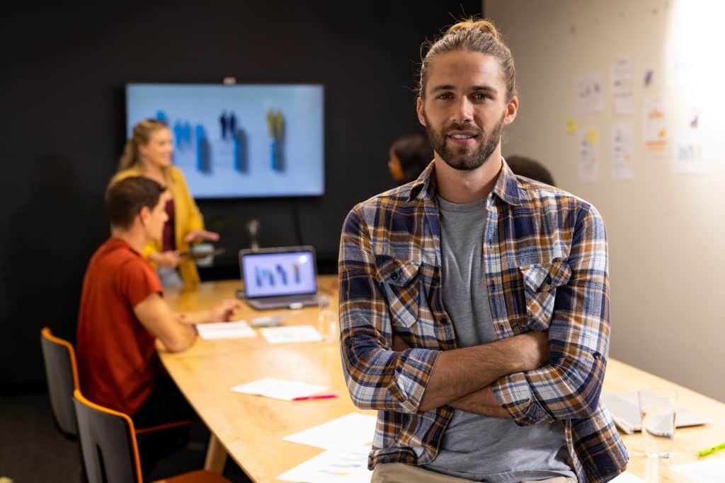 Portrait of happy caucasian casual businessman with hair bun smiling in meeting room